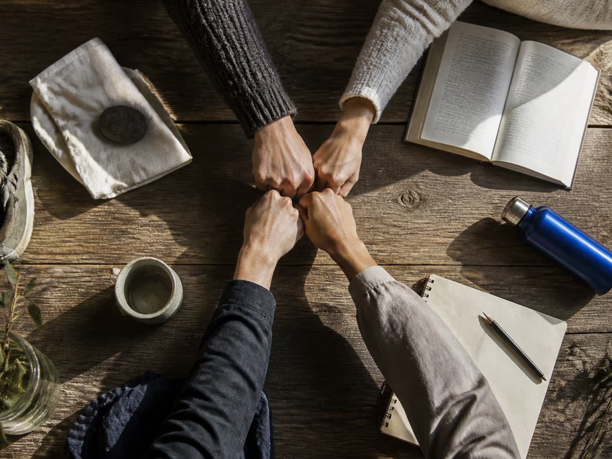 Four friends bring their hands together around a shared table.